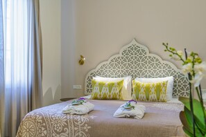 A neatly made bed with patterned bedding and pillows, a decorative headboard, and a bedside table with a lamp. - The Way Inn (Safed)