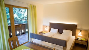 A hotel room with a bed, bedside tables, a desk with chairs, a window with curtains, and a view of trees. - Pension Weihergut (Cermes)