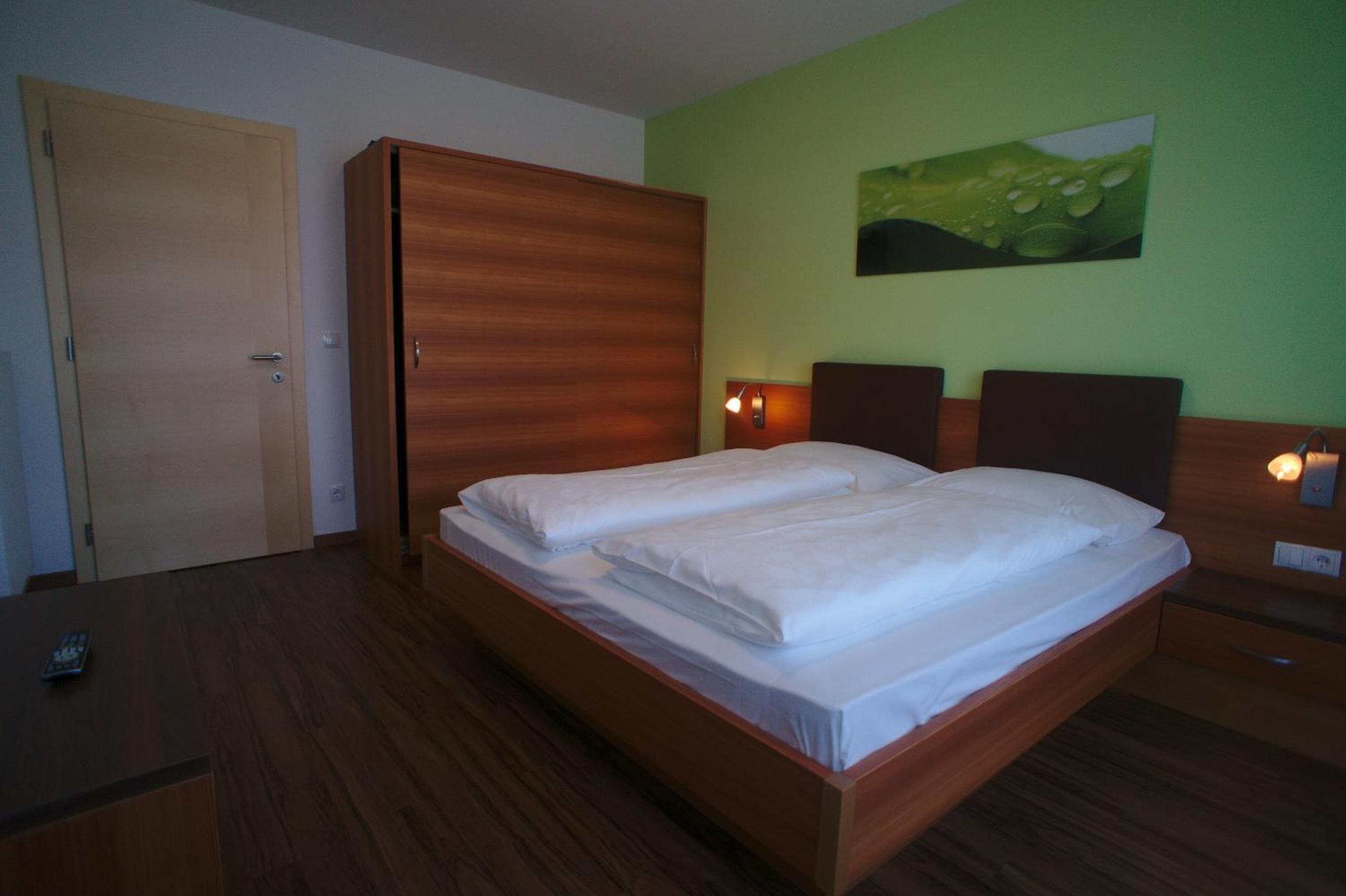 A double bed with a wooden headboard, a green wall, and a painting of a leaf.