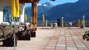 A terrace with wooden furniture, yellow umbrellas, and a view of mountains. - Pension Weihergut (Cermes)