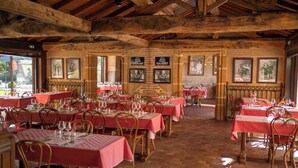 Un restaurante con varias mesas y sillas, vigas de madera en el techo y cuadros en las paredes.