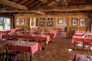Un restaurante con varias mesas y sillas, vigas de madera en el techo y cuadros en las paredes.
