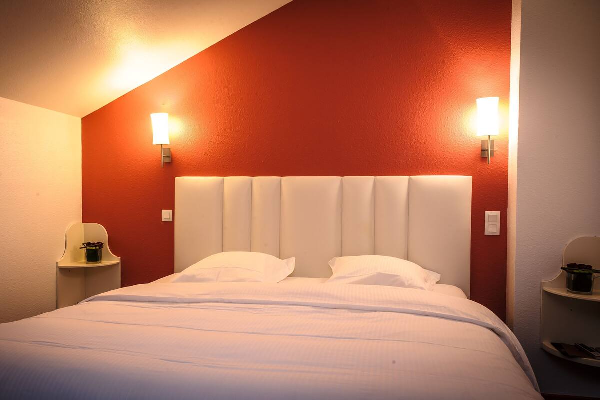 A hotel room with a bed, two bedside tables, and wall-mounted lamps.