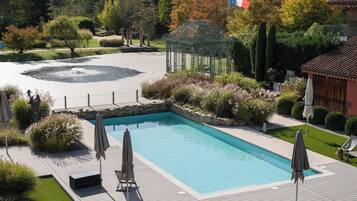 A rectangular swimming pool with a surrounding deck, surrounded by well-maintained landscaping and a French flag.