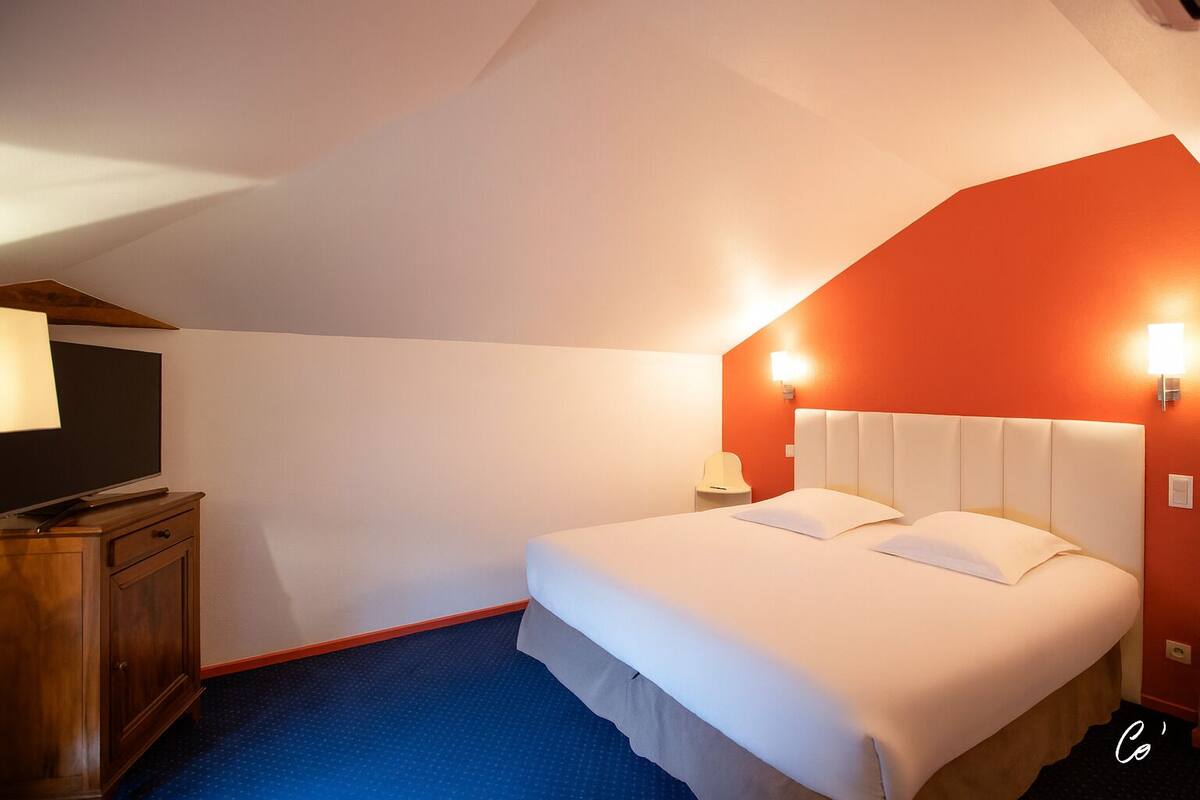 A hotel room with a bed, a TV, a wooden cabinet, and a red accent wall.