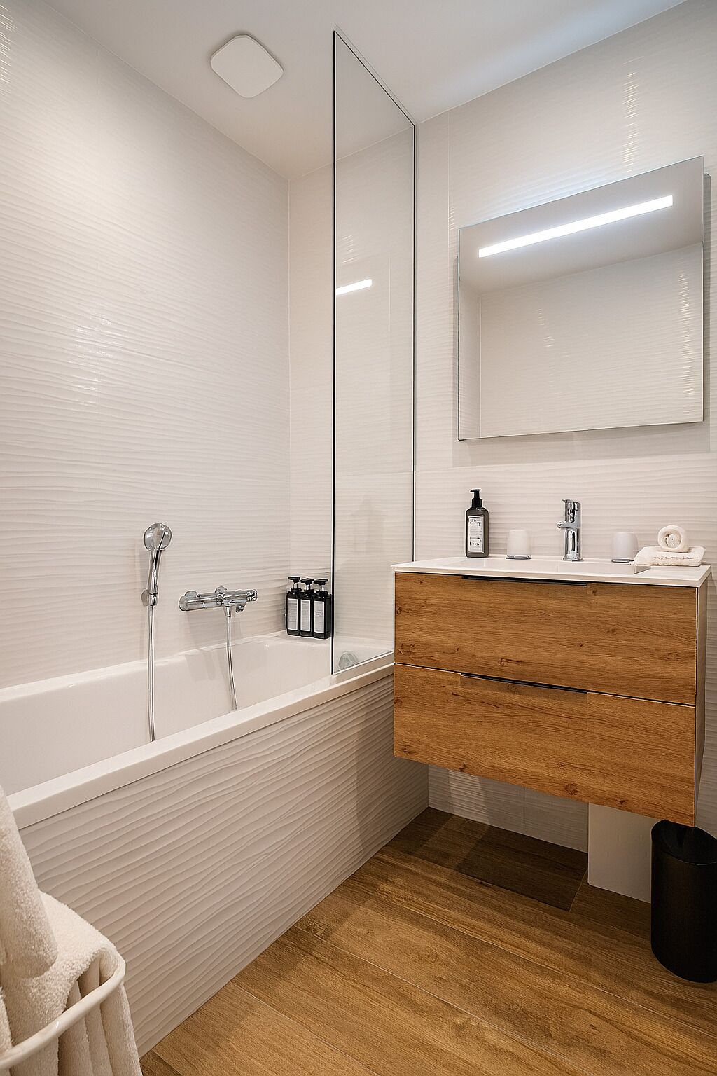 A modern bathroom with a white bathtub, wooden vanity, and a large mirror.