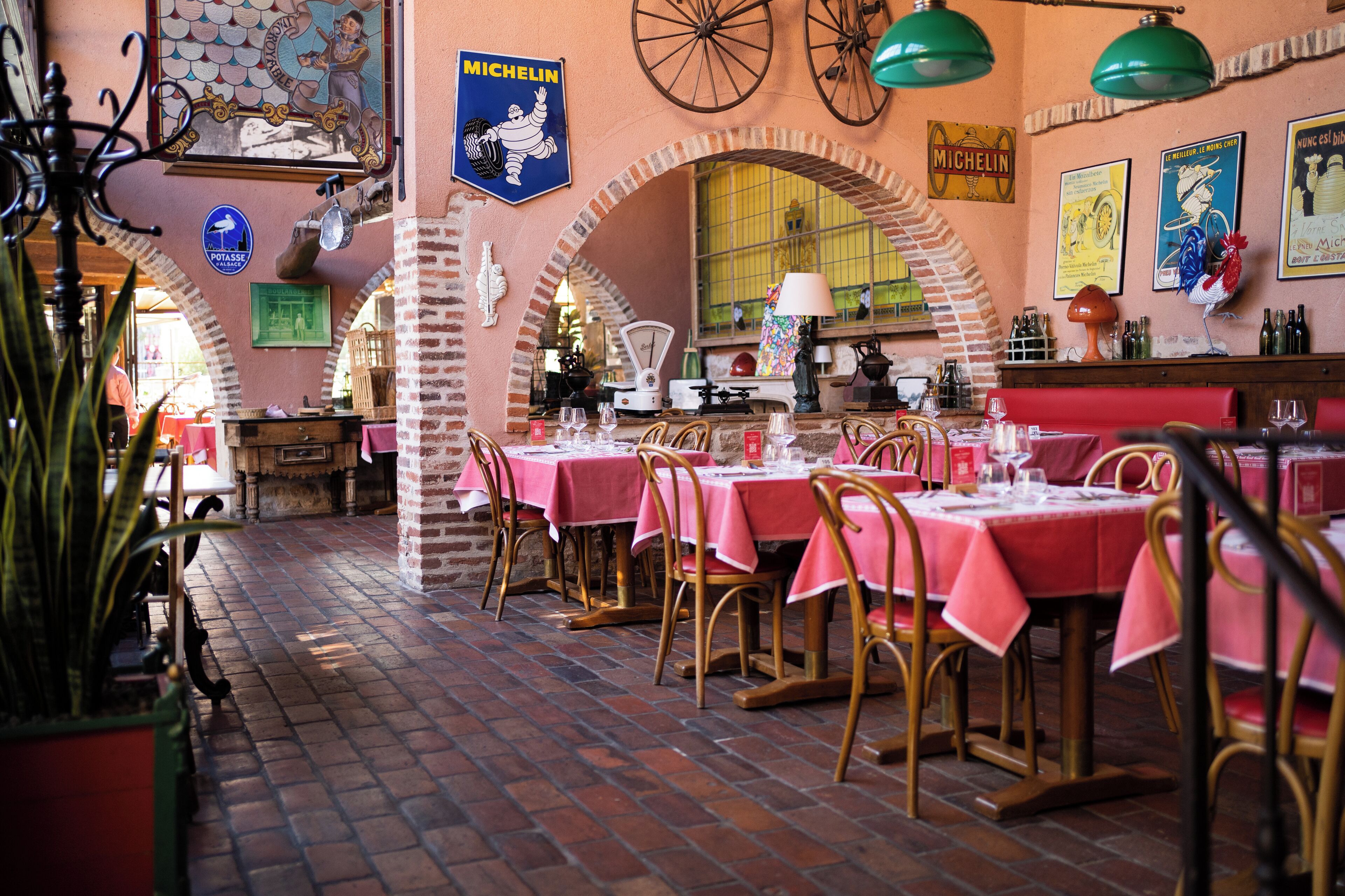 Interior de restaurante con arcos de ladrillo, mesas con manteles rosas y decoración vintage.