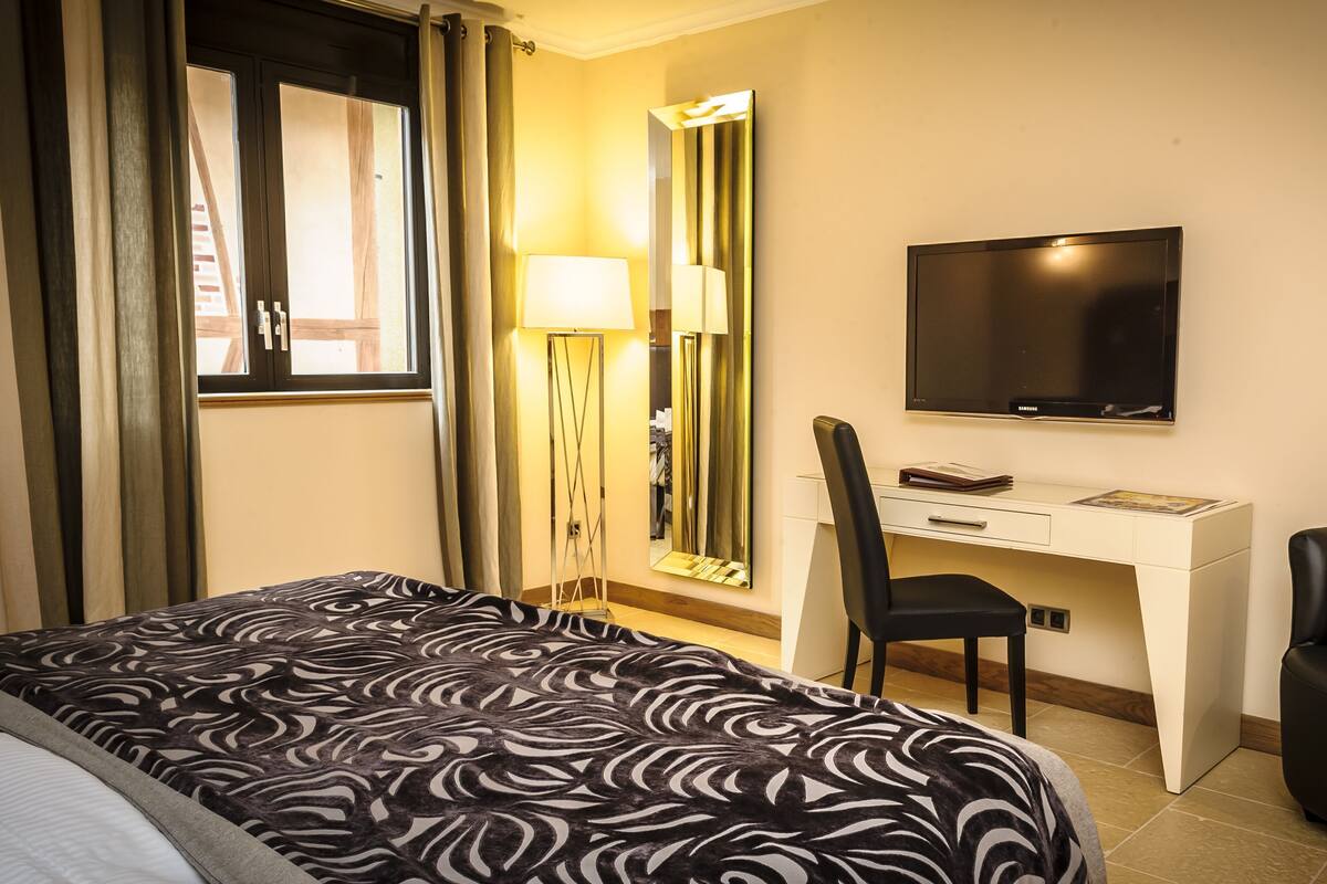 A hotel room with a bed, desk, chair, TV, and a large mirror.