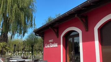 Un bâtiment rouge portant l’enseigne « ESPACE Côte Rivière » et doté d’une terrasse avec des chaises et des tables en osier.
