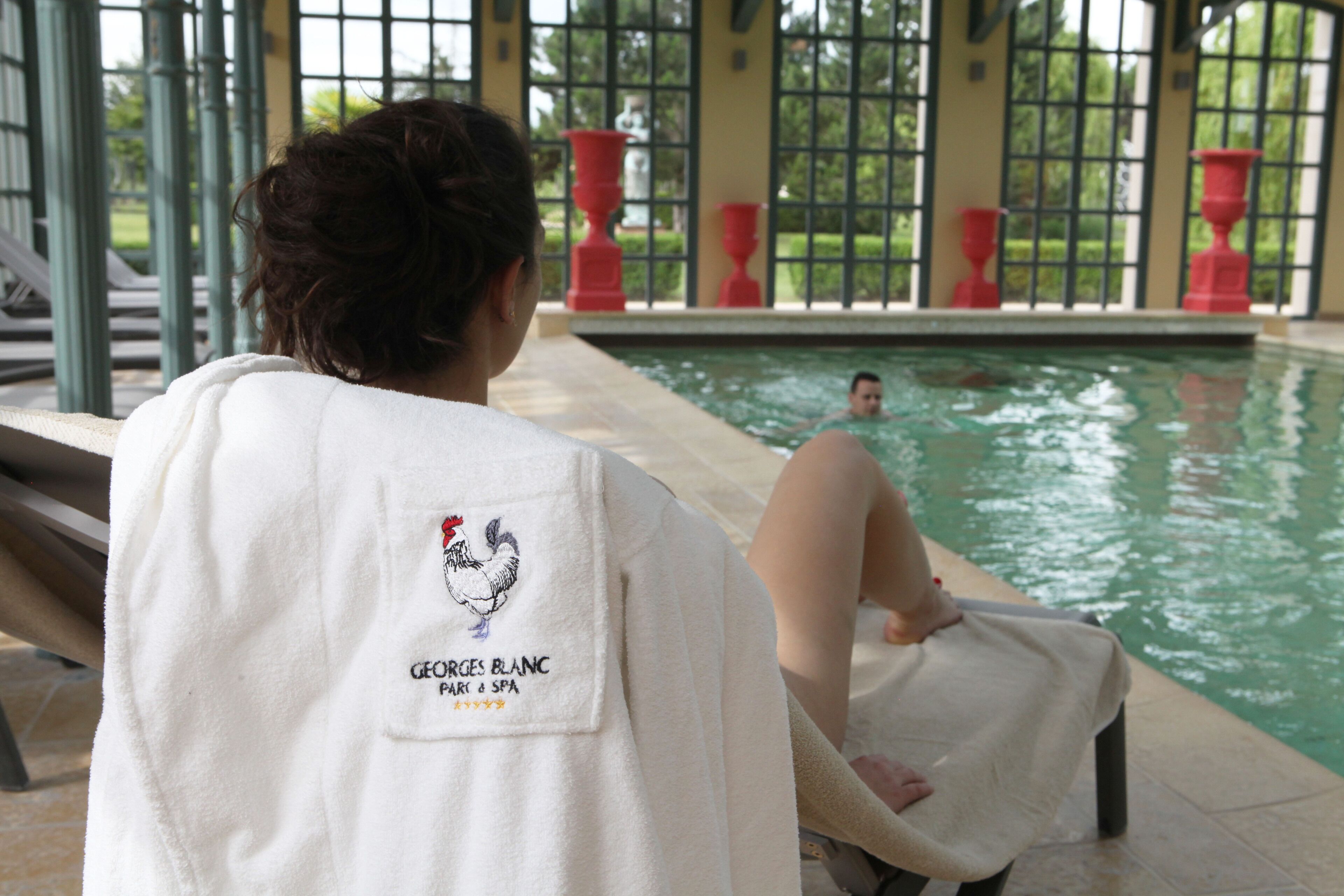 Una persona asseguda al costat d'una piscina, amb una tovallola als hombros, i vista cap a l'exterior.