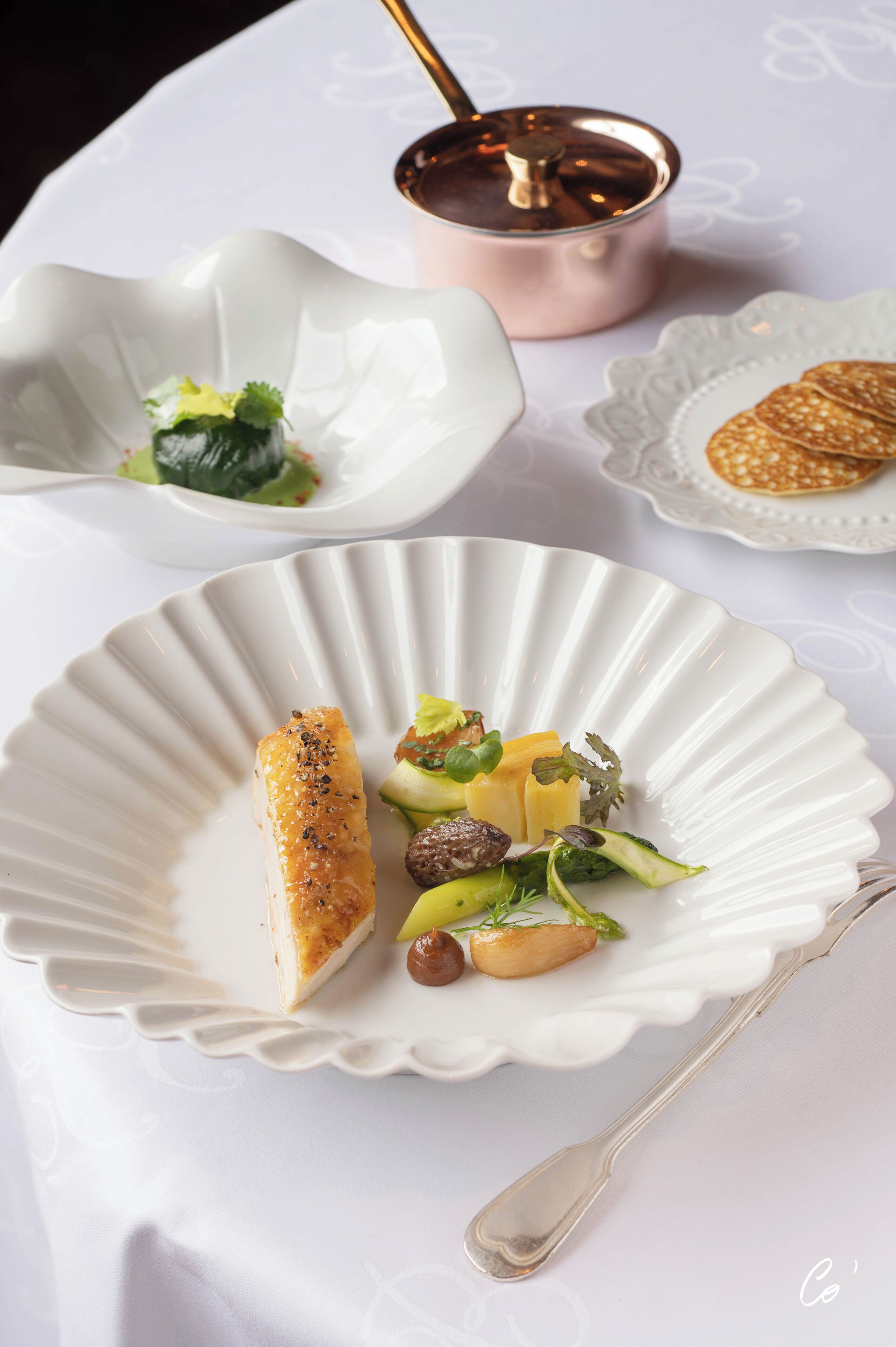 A white plate with a piece of salmon, vegetables, and a small bowl of sauce.