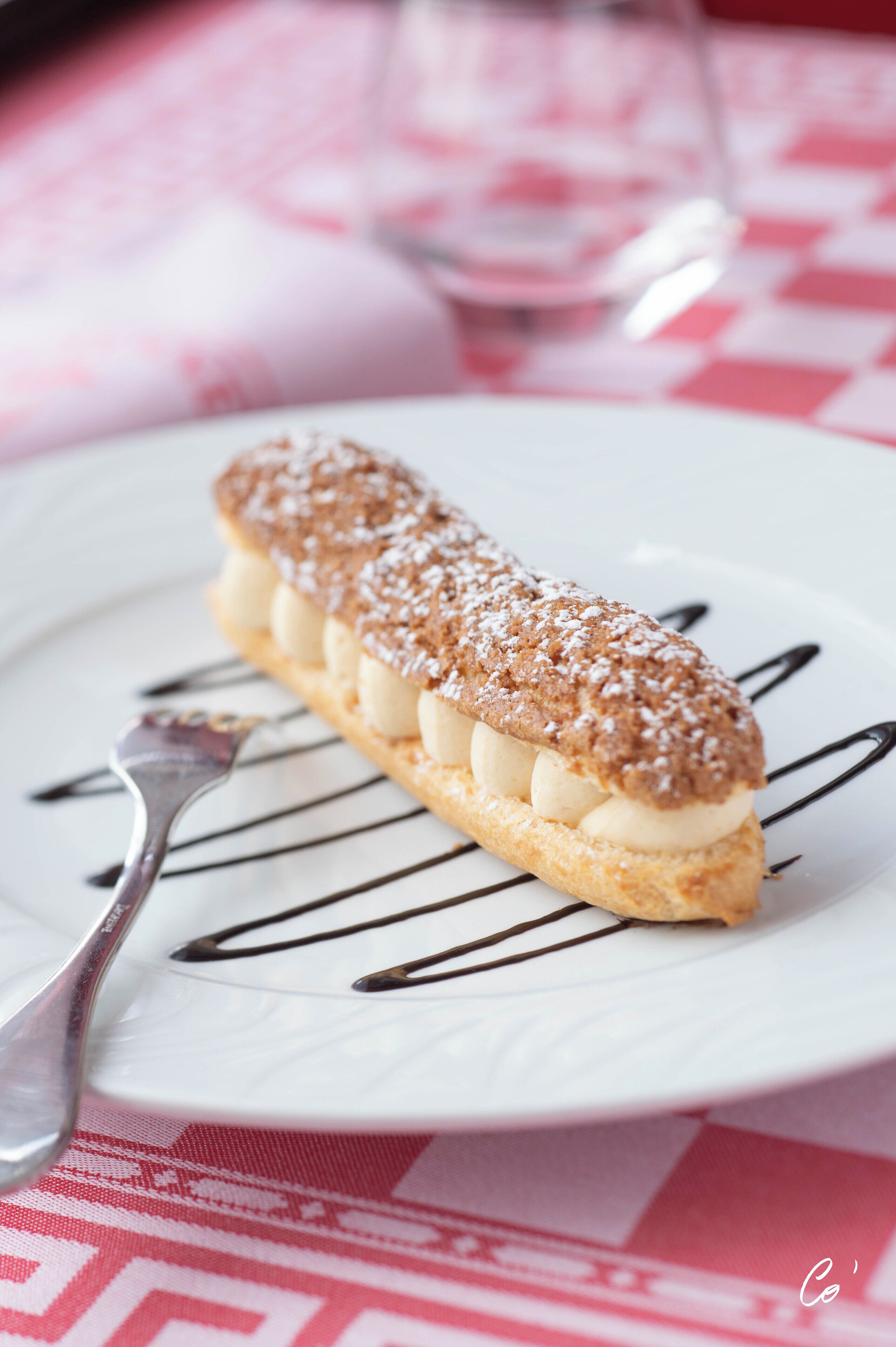 A dessert on a white plate with chocolate drizzle, set on a table with a red and white checkered tablecloth.