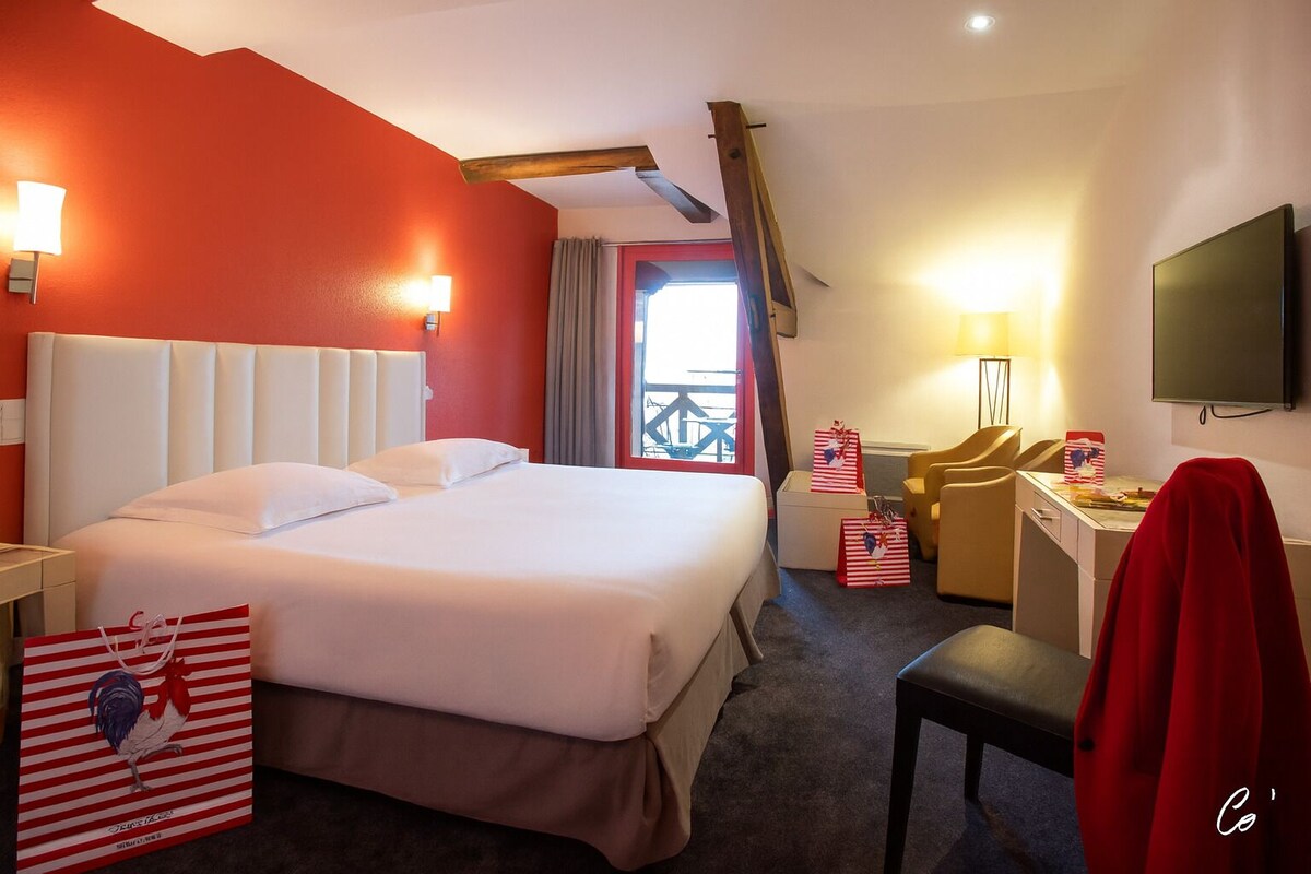 Habitación de hotel con una cama grande, un escritorio con silla, televisión y ventana con cortinas.