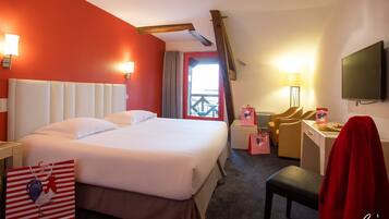 Habitación de hotel con una cama grande, un escritorio con silla, televisión y ventana con cortinas.