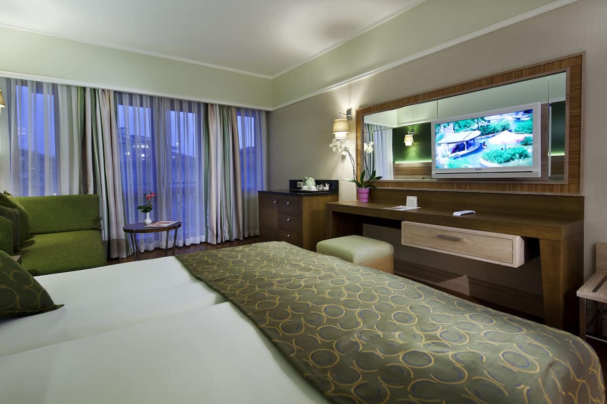 Habitación de hotel con una cama grande, un escritorio con televisor de pantalla plana, una silla y una mesita con un jarrón de flores.