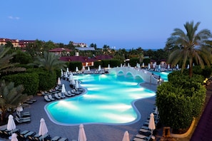 A resort pool with lounge chairs and umbrellas, surrounded by palm trees and buildings. - Club Grand Side Amazon Water World - All Inclusive (Manavgat)