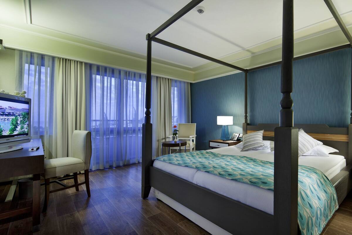 Una habitación de hotel con cama con dosel, un escritorio con lámpara, un televisor y una silla.