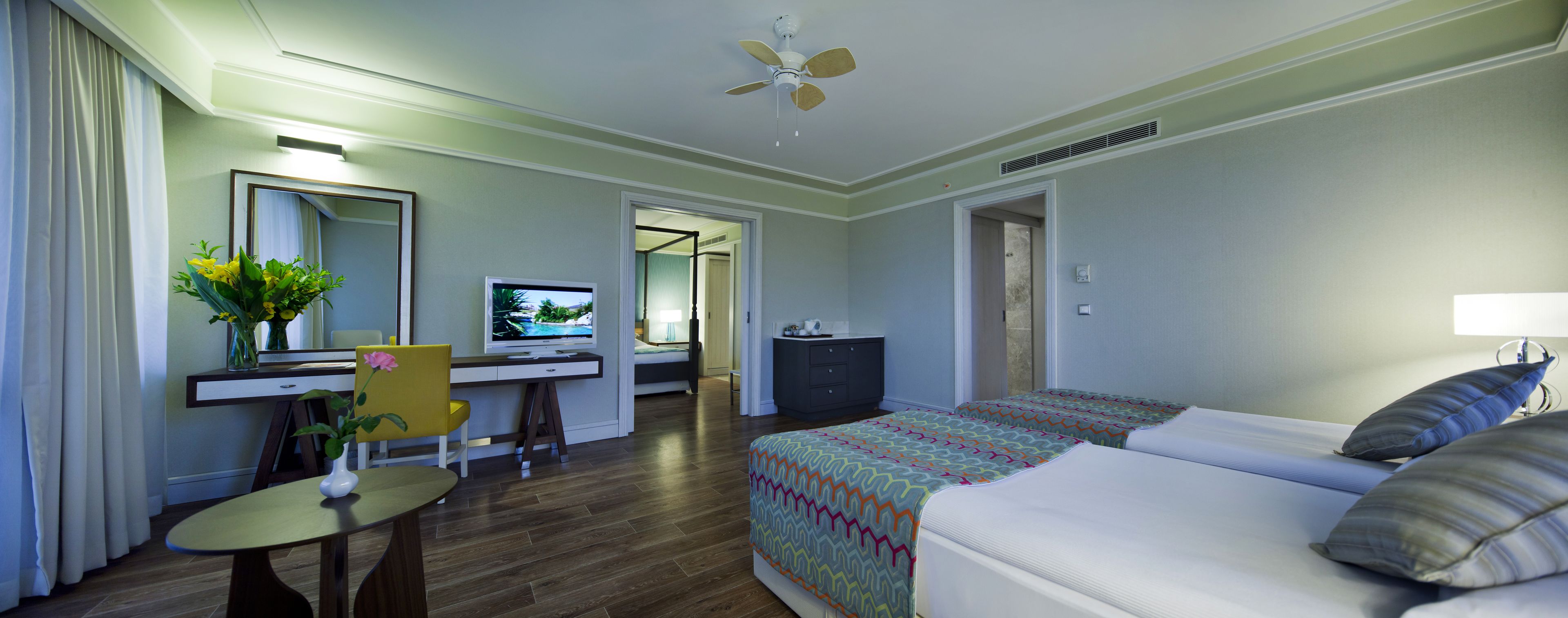 A hotel room with a bed, desk, chair, TV, and a small table with a vase.