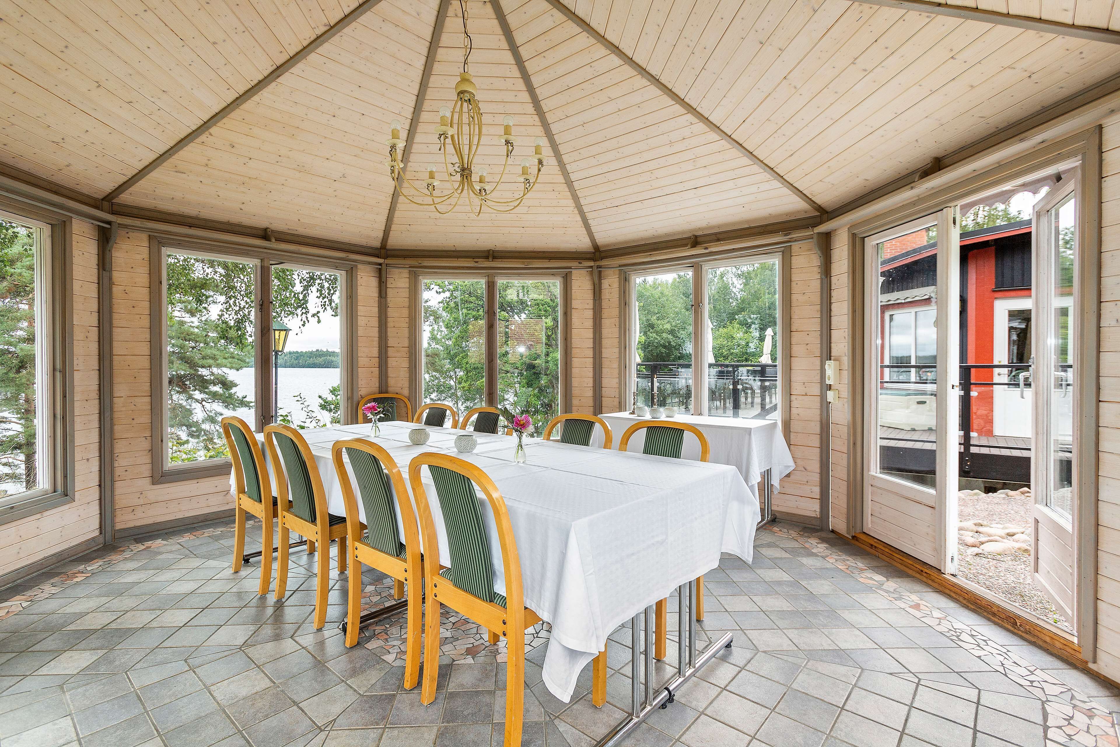 A covered dining area with a table set for six, large windows, and a view of a lake.
