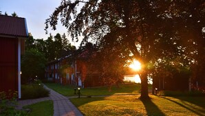 A pathway leading to a building with a red facade, surrounded by grass and trees, with the sun setting in the background. - Hotel Ullinge, Sure Hotel Collection by Best Western (Eksjo)