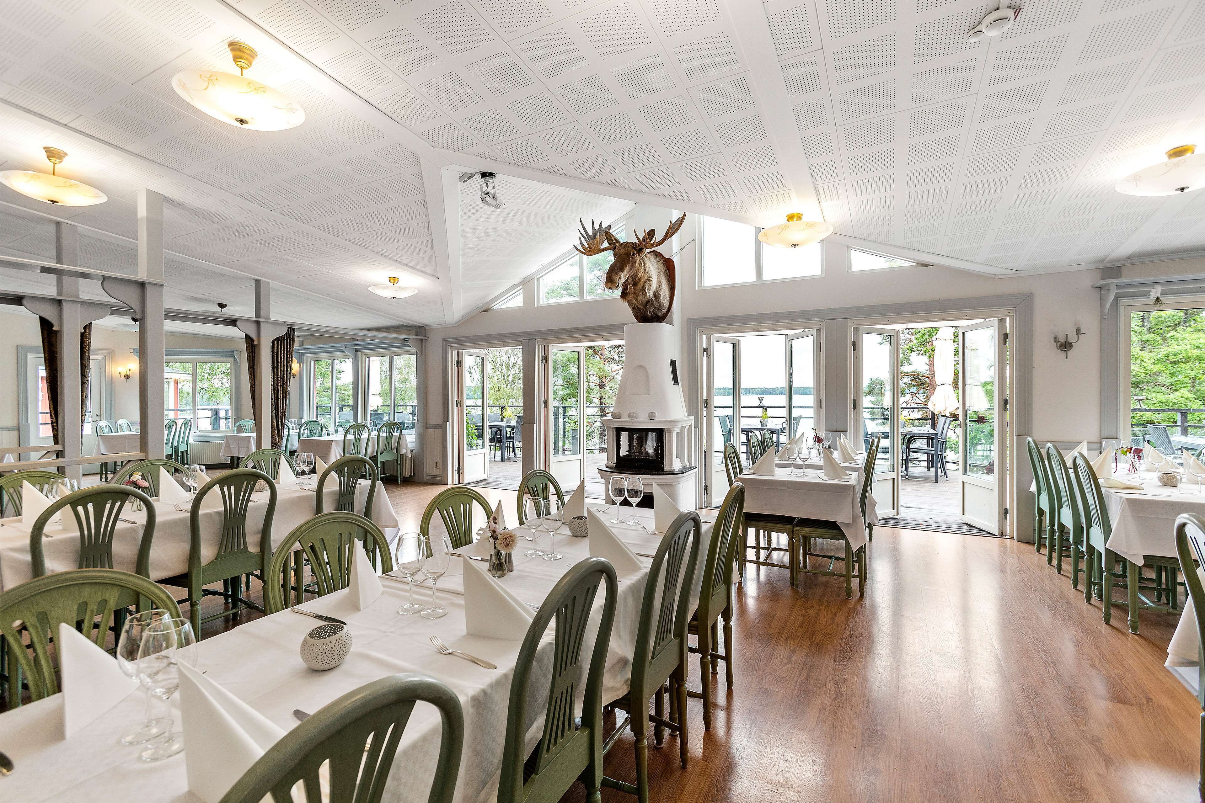A restaurant with high ceilings, green chairs, and a central fireplace.