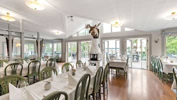 A restaurant with high ceilings, green chairs, and a central fireplace.