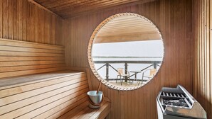 A wooden sauna with a circular mirror, a bench, a bucket, and a grill. - Hotel Ullinge, Sure Hotel Collection by Best Western (Eksjo)