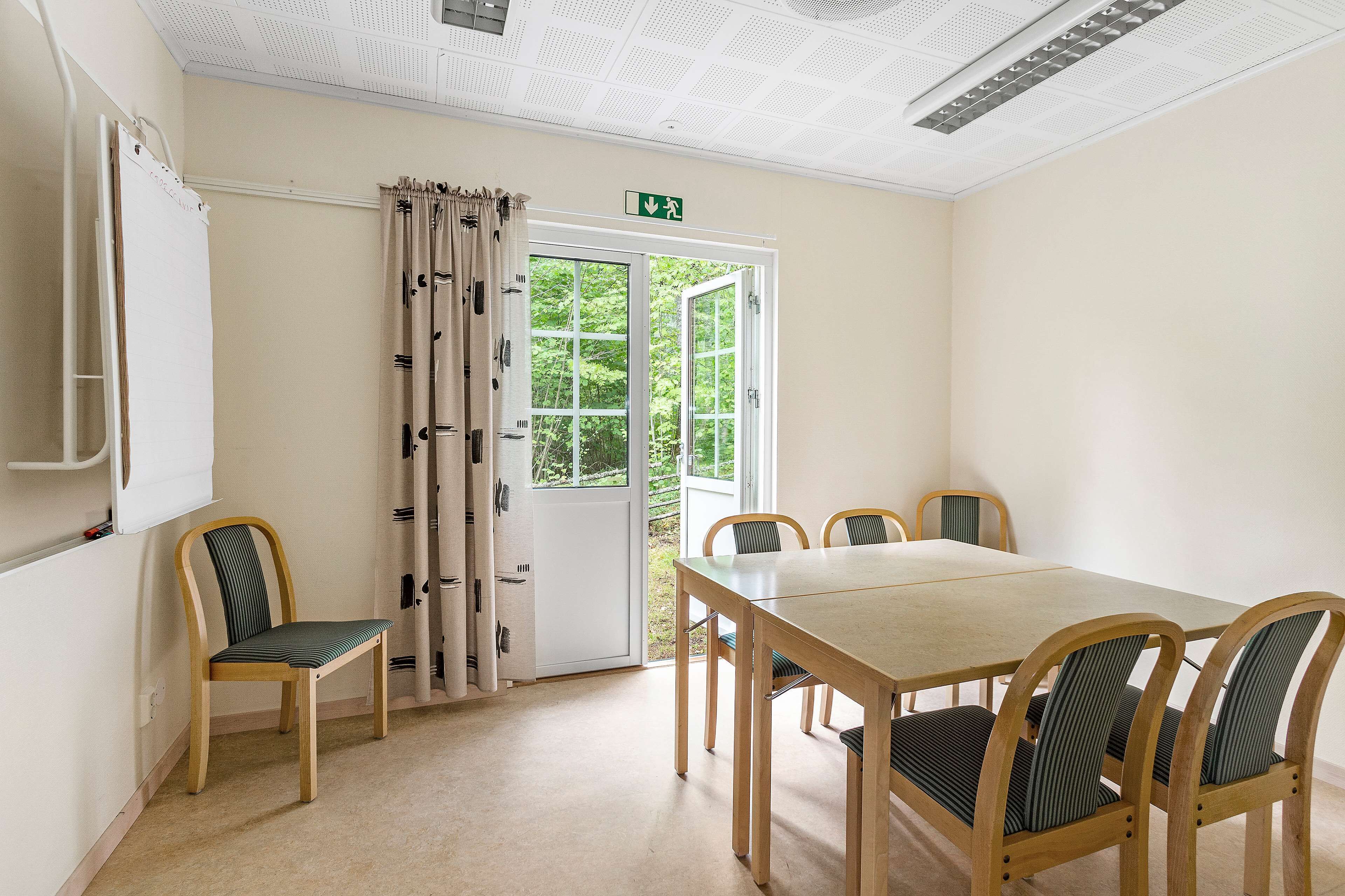 A dining area with a table and chairs, a whiteboard, and a door with a curtain.