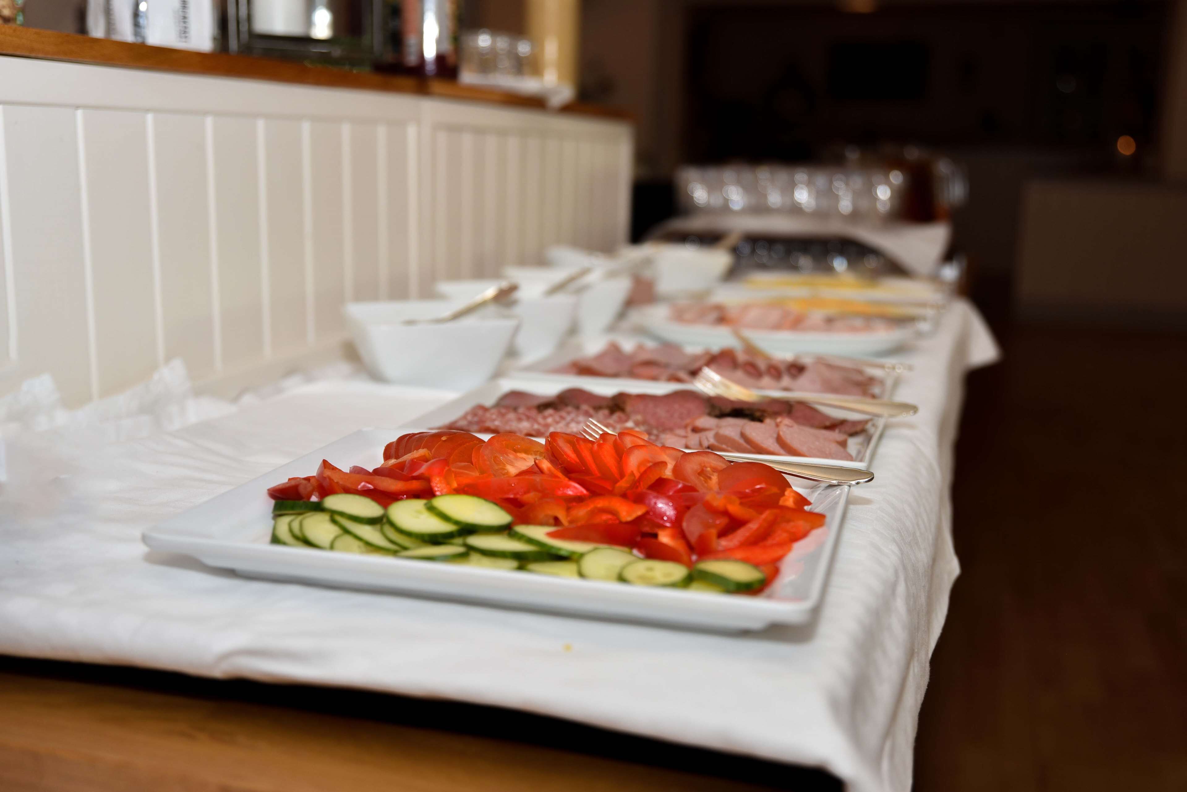 A buffet table with various food items including sliced cucumbers, tomatoes, and meats.