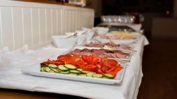 A buffet table with various food items including sliced cucumbers, tomatoes, and meats.