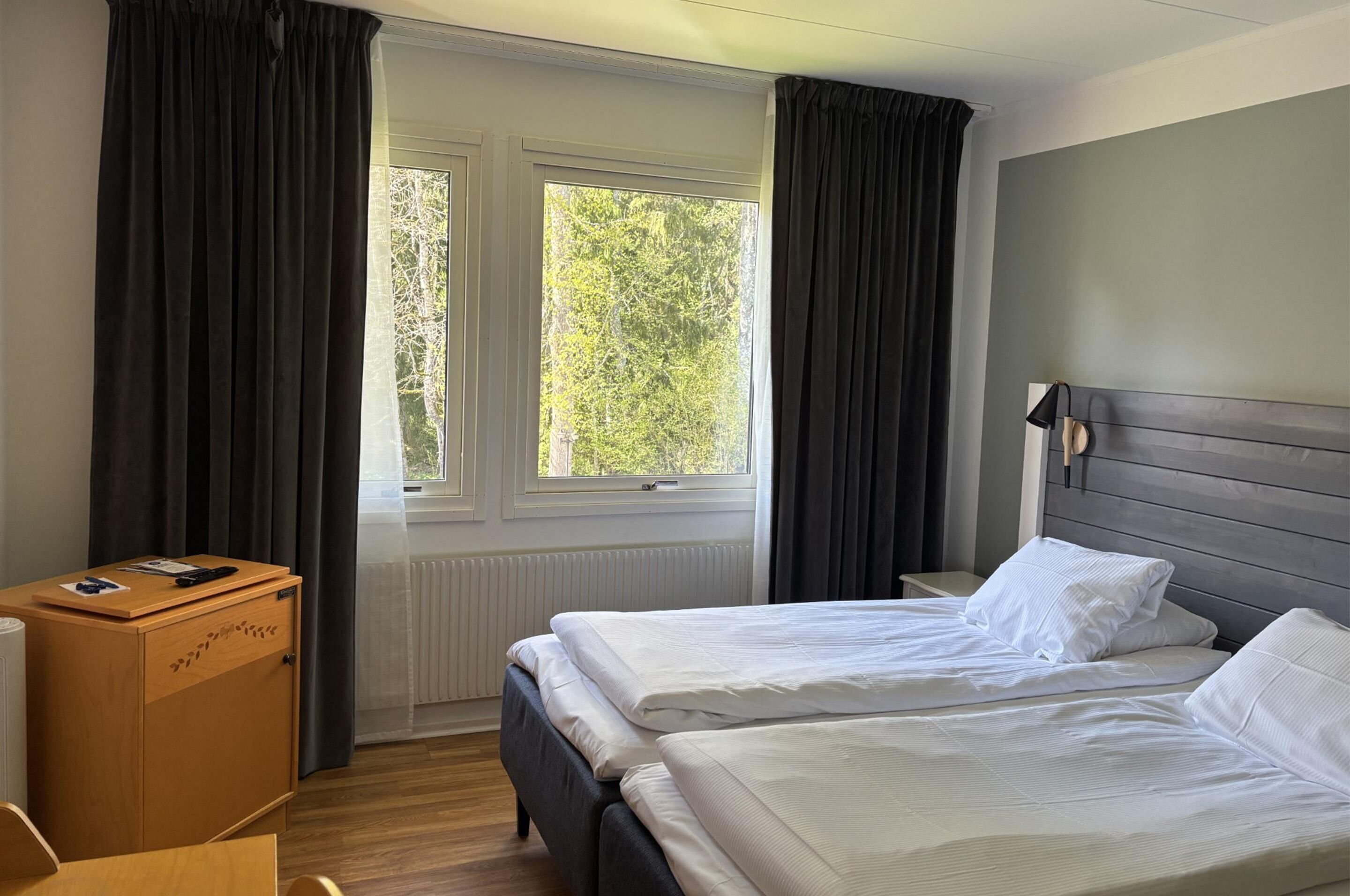 Ein Hotelzimmer mit zwei Betten, einem Holzschrank und einem Fenster mit Vorhängen.