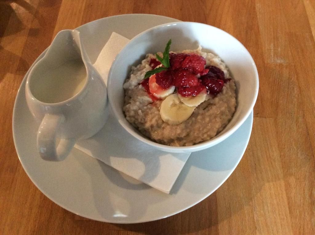 Un tazón de avena con bayas y una pequeña jarra de leche sobre un plato blanco.