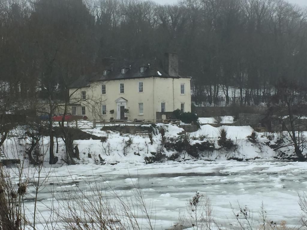 Un grande edificio a due piani con una facciata simmetrica, circondato da terreno e alberi innevati.