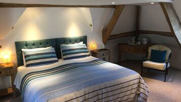 A bedroom with a large bed, two bedside tables, a chair, and a small table with a lamp.