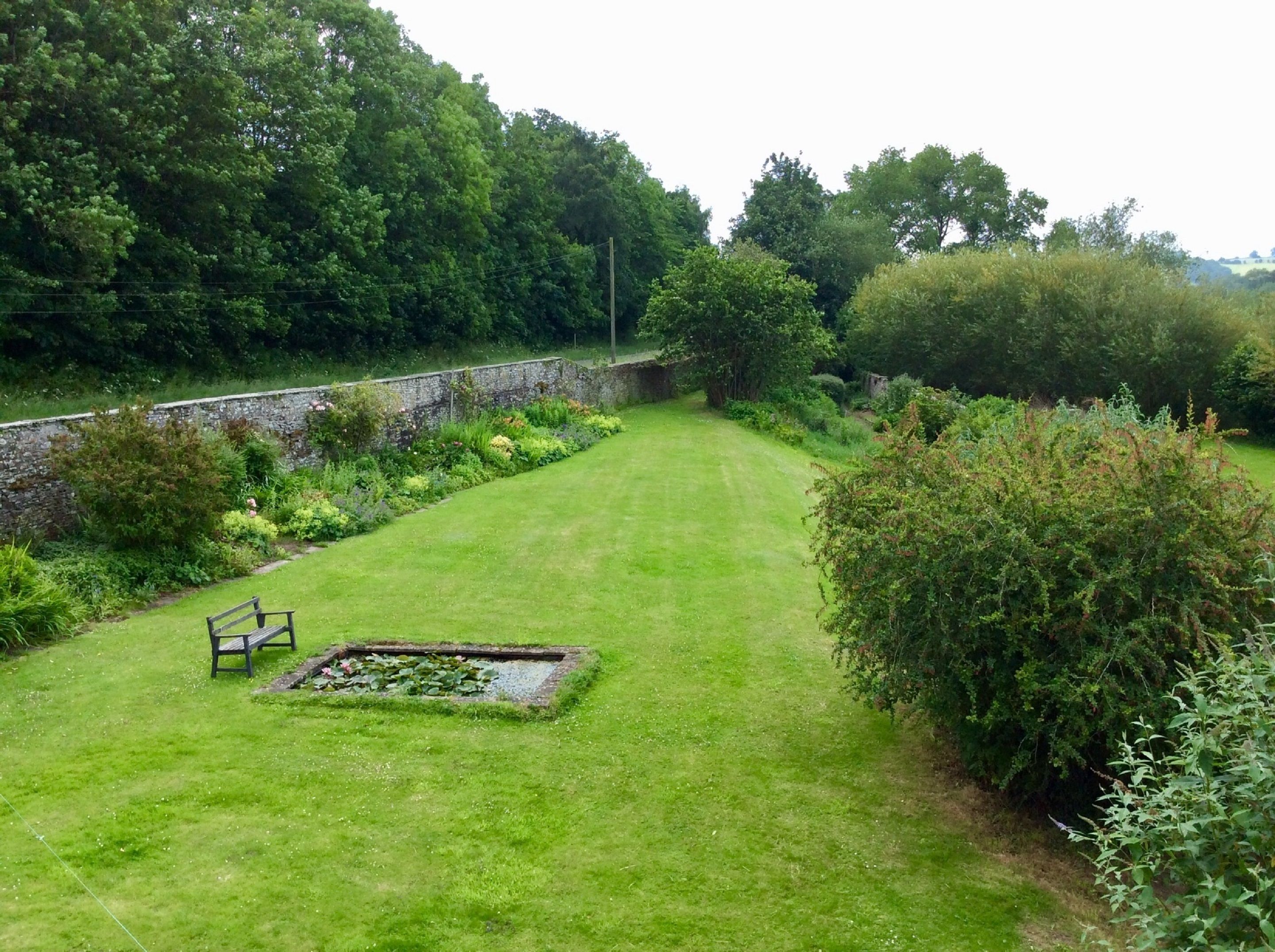 A well-maintained garden with a paved area, a bench, and a pond.
