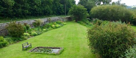 A well-maintained garden with a paved area, a bench, and a pond.