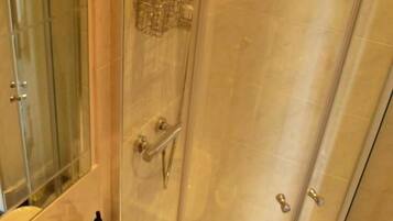 Ducha envuelta en vidrio con cabezal de ducha manual y dispensador de jabón de vidrio.