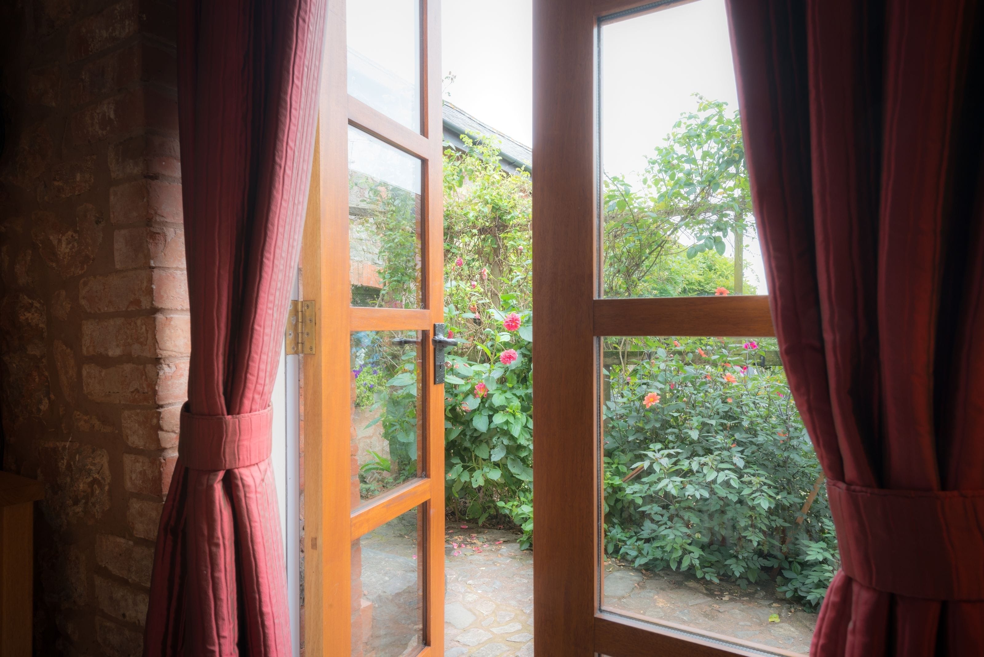 An open wooden door leading to a garden with a brick wall and a stone pathway.