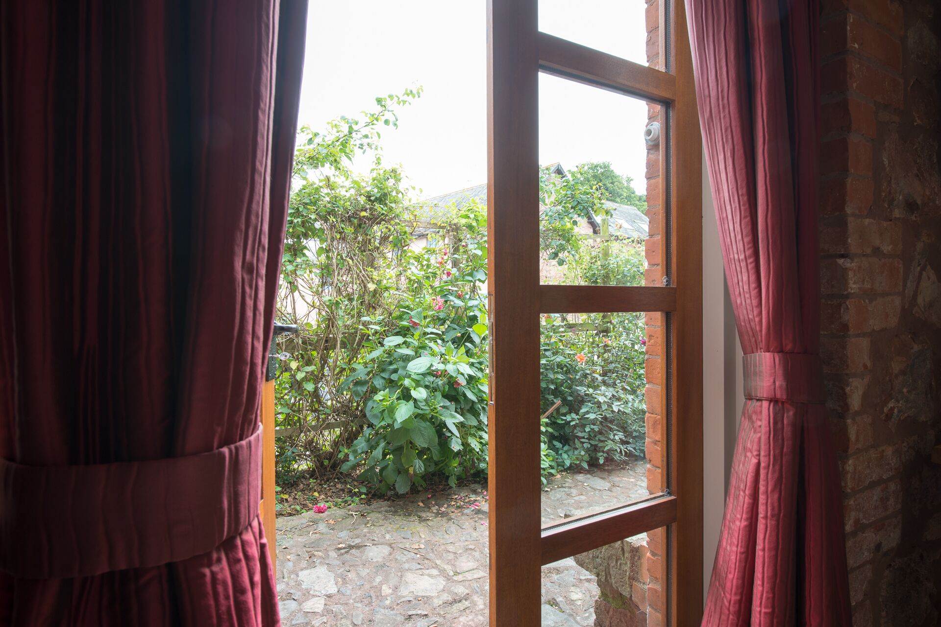 Una ventana con vista a un jardín y un muro de ladrillo.
