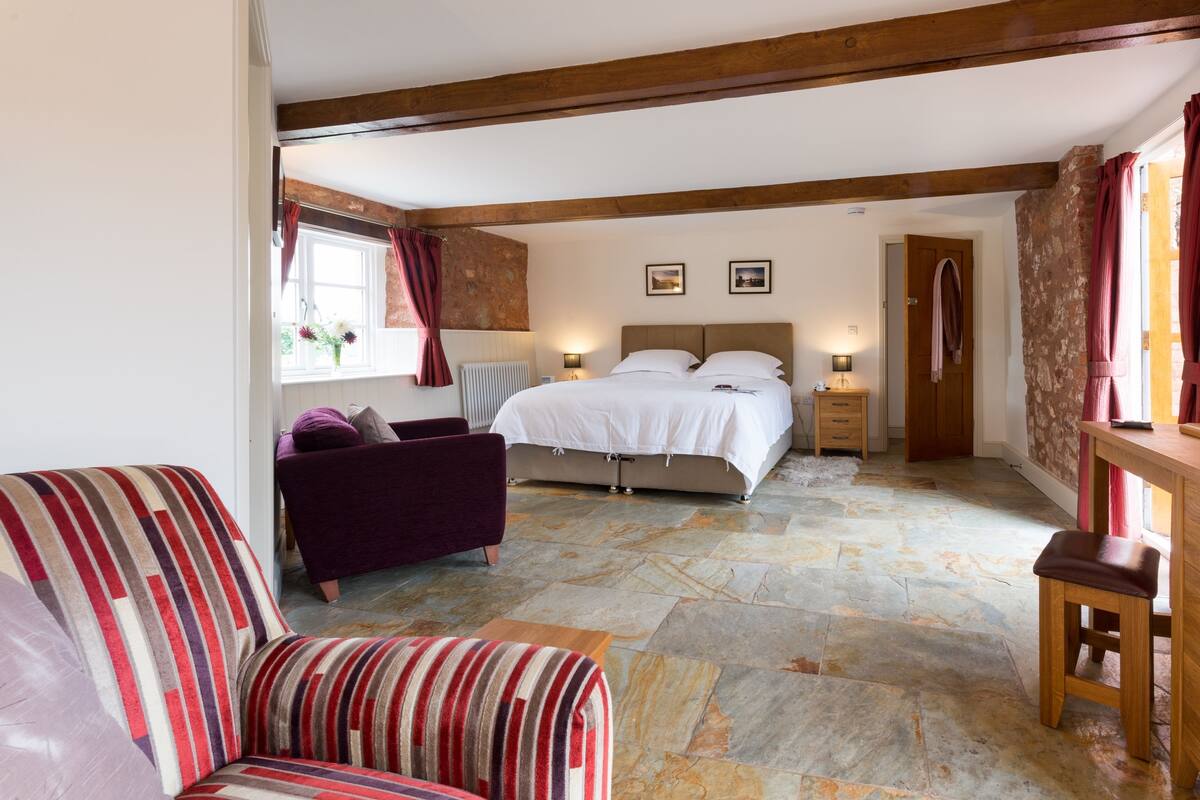 Quarto com cama, cadeira, mesa de cabeceira e porta de madeira.