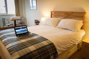 Una habitación de hotel con una cama, una computadora portátil sobre la cama, una mesita de noche, una lámpara, una silla y una ventana.