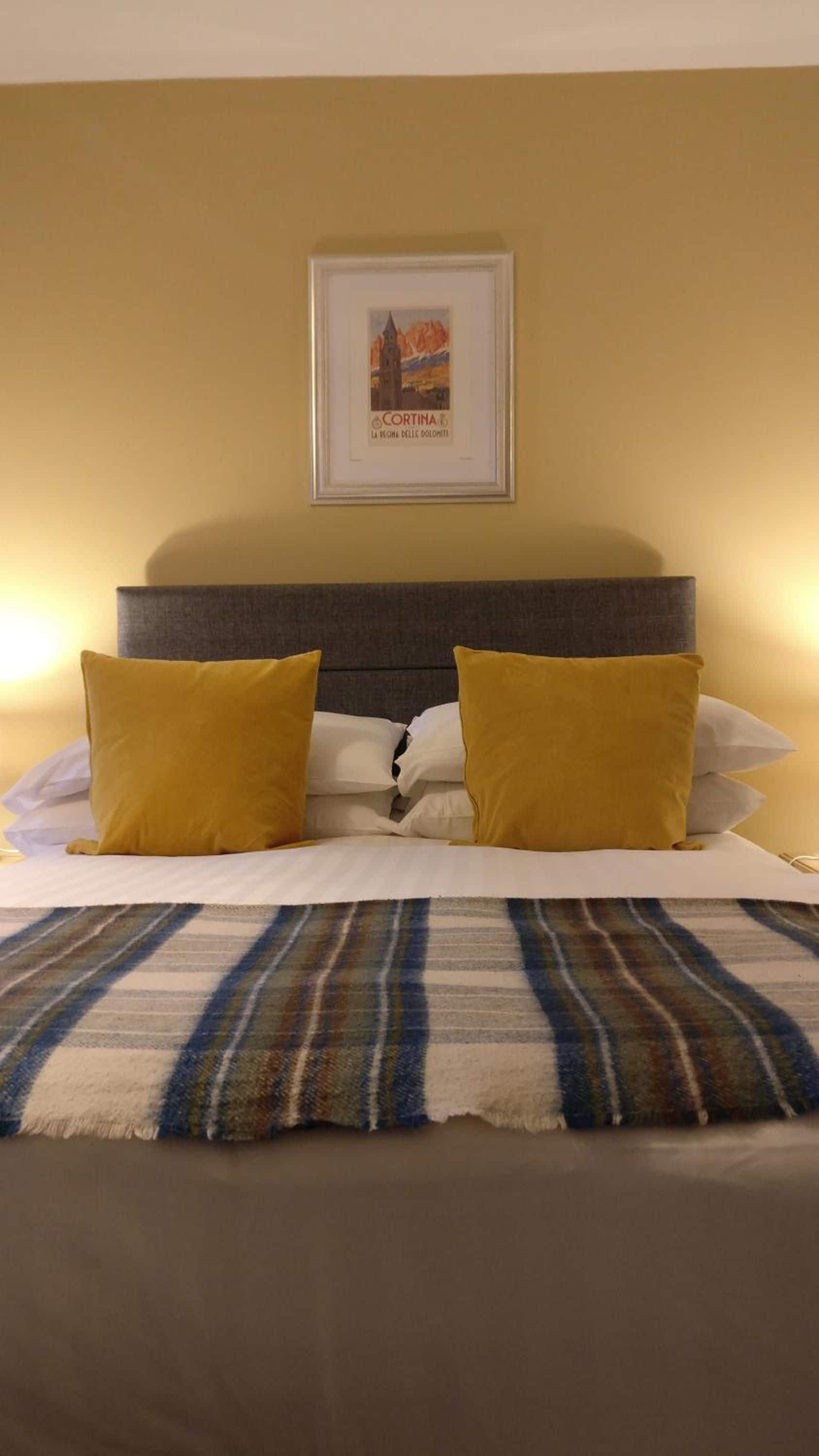 A hotel room with a bed, two pillows, a framed picture on the wall, and a striped blanket.