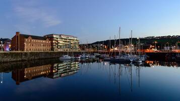 A marina with boats docked, a building with multiple floors, and a calm water body reflecting the structures.