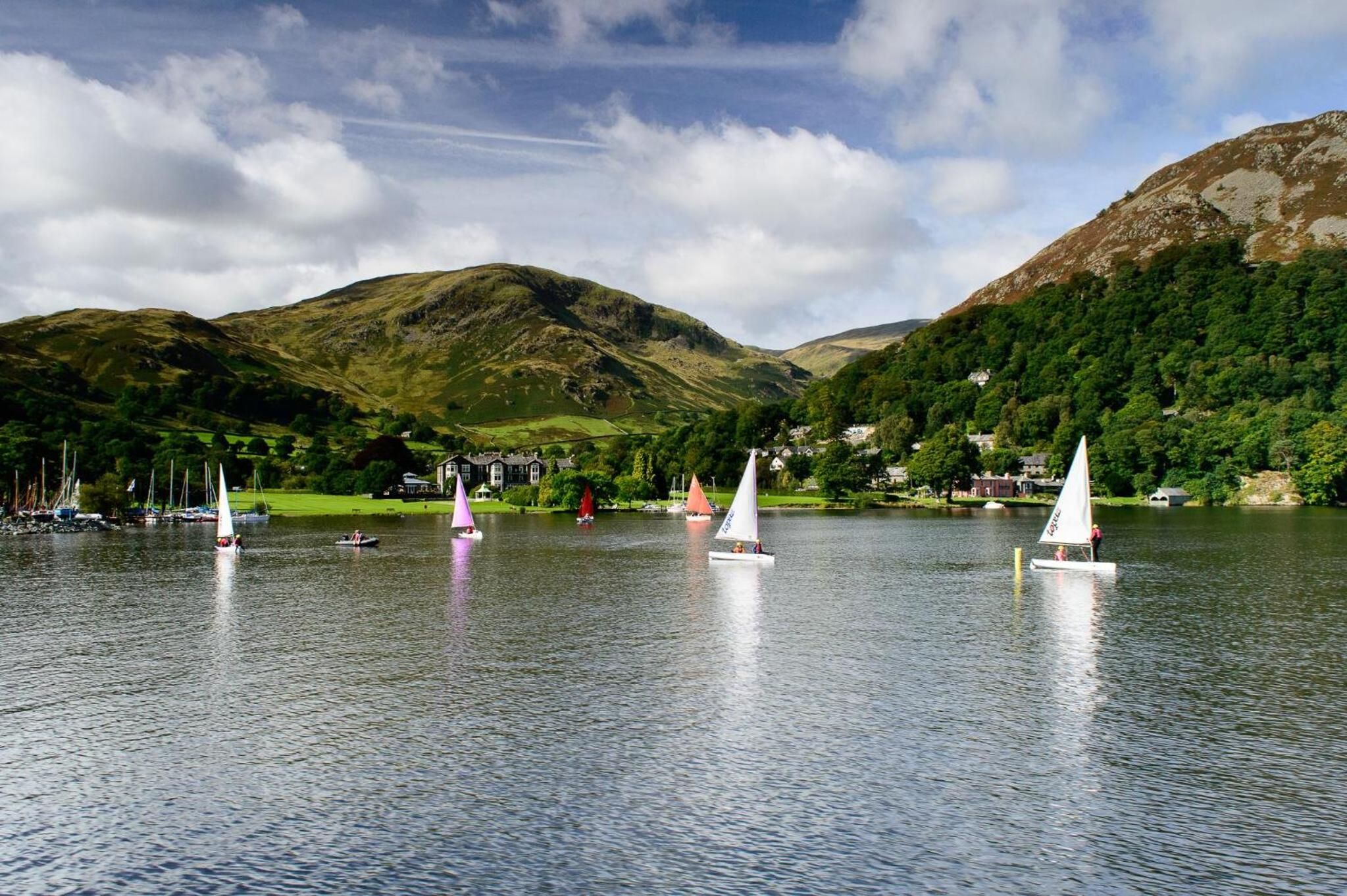 A lake with sailboats, surrounded by hills and houses.