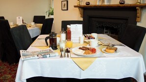 A dining table set with breakfast items, a newspaper, and a menu. - The Mansion Bed & Breakfast (Whitehaven)