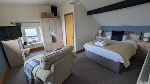 A bedroom with a bed, a chair, a wardrobe, a television, and a window. - The Mansion Bed & Breakfast (Whitehaven)
