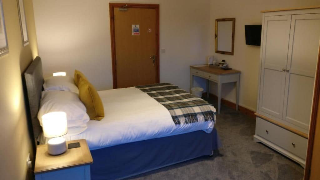 A bedroom with a bed, bedside table, lamp, wardrobe, and a desk.