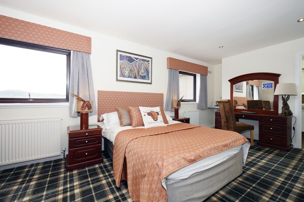 A hotel room with a bed, a desk, a chair, a dresser, and a window with curtains.