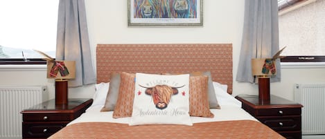 A hotel room with a patterned bedspread, a framed artwork above the bed, and a view of the mountains through the window.