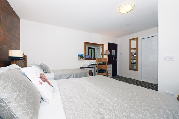 A hotel room with two beds, a desk, a chair, a mirror, and a wardrobe.